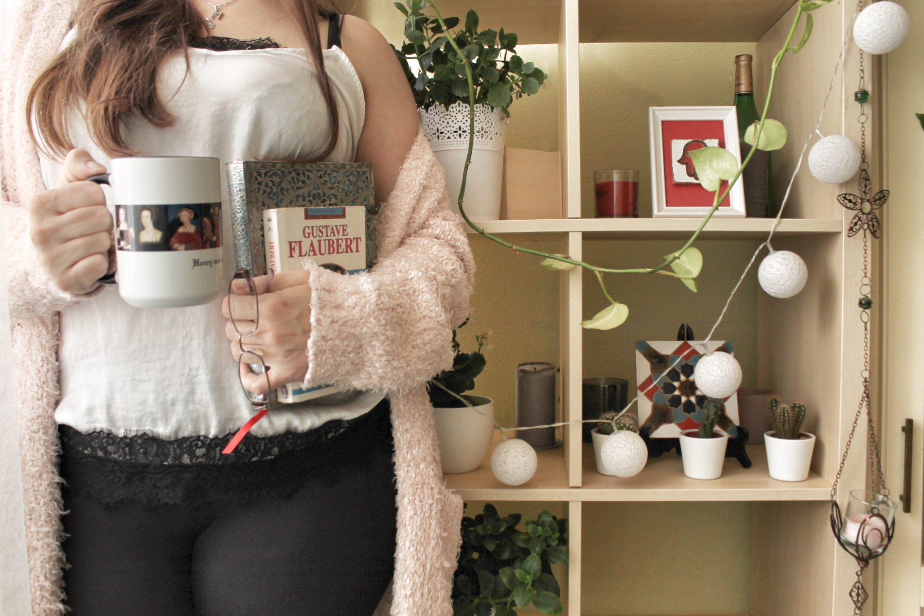 Retrato de la autora con una taza de Enrique VIII, un cuaderno y Madame Bovary, frente a una estantería con plantas